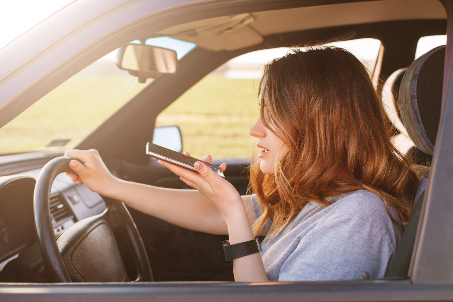 A photograph shows a young woman talking on a smartphone while driving.